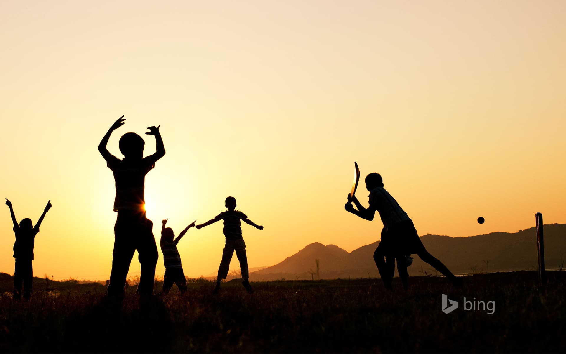Bing Wallpaper: Silhouette of young Indian boys playing cricket against a sunset background